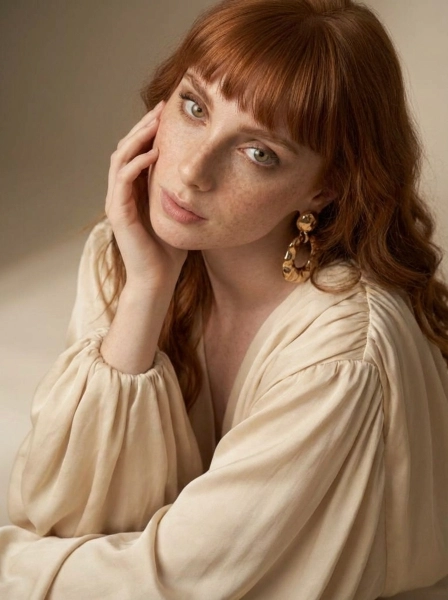 A_woman_with_long_wavy_red_hair_with_bangs_wearing-1774540741856